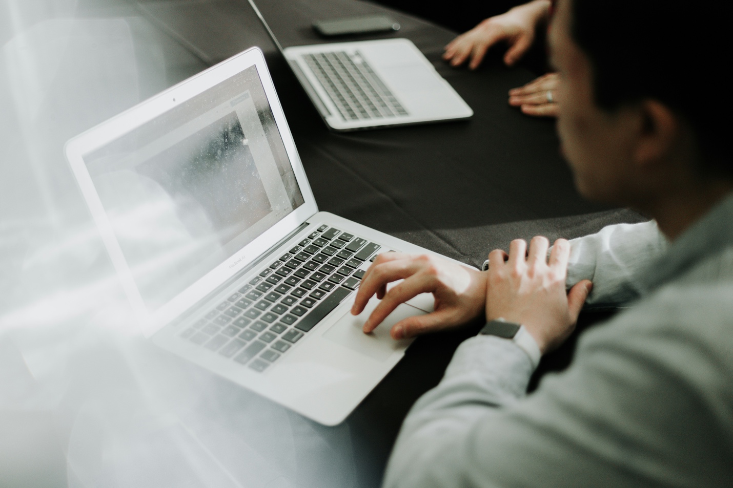 Person using laptop at desk with another laptop nearby